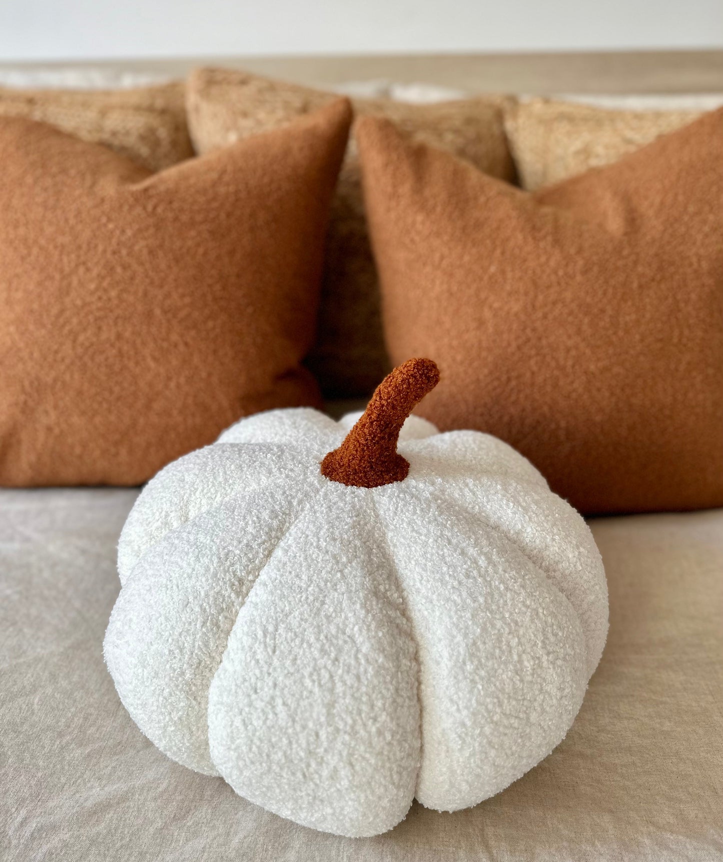 White textured pumpkin with a brown stem on a beige surface with brown cushions in the background